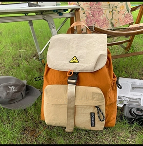Outdoor backpack detail showing orange and beige color block nylon with a smiley embroidery