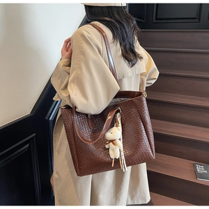 Detailed side view of a woven tote bag with a plush bear charm and silk scarf accent