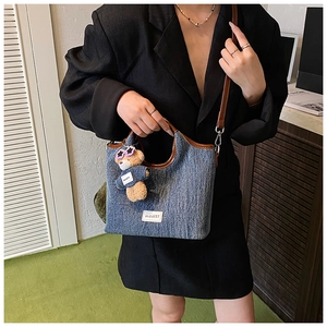 Close-up of denim shoulder bag with brown leather trim and cute plush bear charm