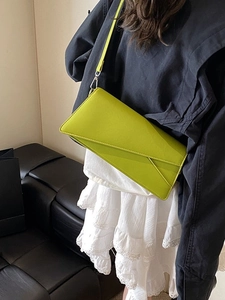 Neon green envelope crossbody bag with geometric flap worn by model in a soft home setting