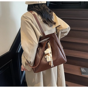 Detail of dark brown woven leather tote bag with small bear charm on model shoulder