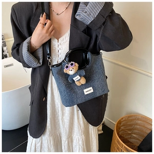 Blue denim tote bag detail featuring a teddy bear charm and sleek black curved handles