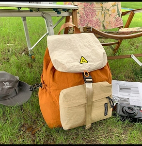 Outdoor camping scene showing a stylish orange and white nylon backpack on a folding table