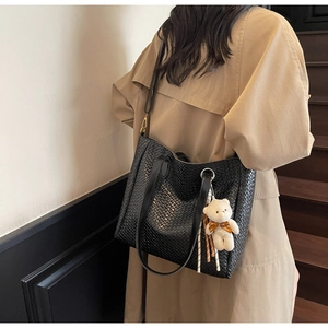 Detail of black woven leather tote bag with bear charm shown on model's shoulder