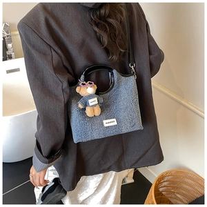Detail of light blue denim bucket bag with teddy bear charm and black circular handle