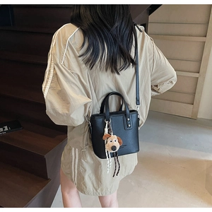 Close-up of black lychee texture crossbody bucket bag with cute dog plush keychain charm