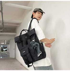 Detail of black roll-top backpack with buckle pockets and a cute plush frog pendant