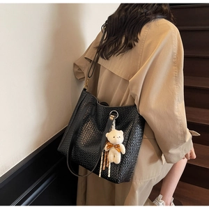 Detail of black woven tote bag featuring a cute plush bear pendant and matte leather texture