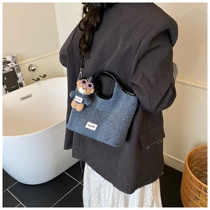 Close-up of blue denim tote bag with black glossy handles and a cute bear bag charm