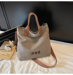 Detail of grey canvas tote bag with brown straps and XOG embroidery in office setting