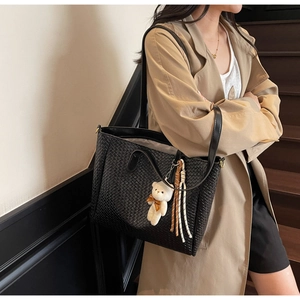 Fashionable black woven tote bag shown on shoulder with cute bear charm and tassel