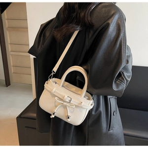 Detail of cream crossbody bucket bag with bow and silver star pendants on leather