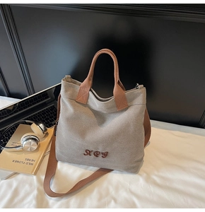 Detail of grey canvas tote bag with brown straps showing embroidery and shoulder strap