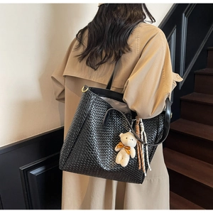 Detail of a black woven tote bag with a plush bear charm worn with a stylish trench coat