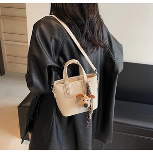 Detail of cream-white pebble grain bucket bag with a cute brown plush dog charm
