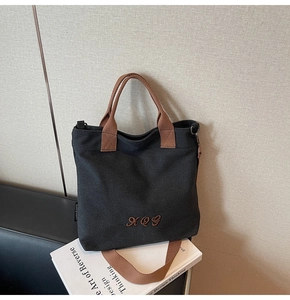 Detailed view of black canvas tote bag with brown XQG embroidery and sturdy handles