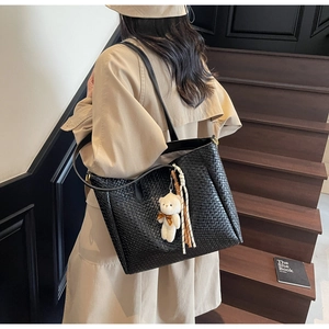 Close-up of black woven tote bag featuring a cute bear charm and striped rope detail