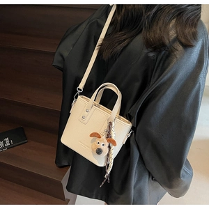 Detail of off-white lychee leather bucket bag with dog plush pendant and checkered scarf