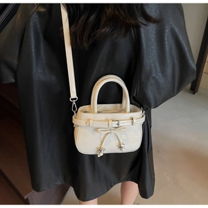 Detail of cream white faux leather bucket bag with bow charm worn by a model