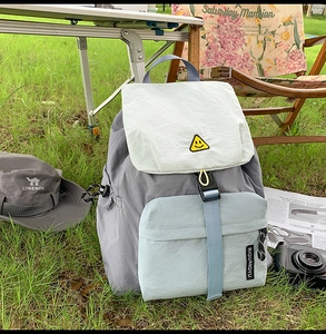 Detailed view of the multi-color nylon backpack with smiley badge in an outdoor setting