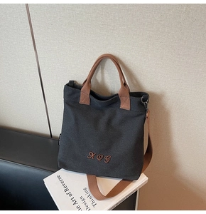 Detail of canvas tote bag showing black fabric with brown straps and XQG embroidery