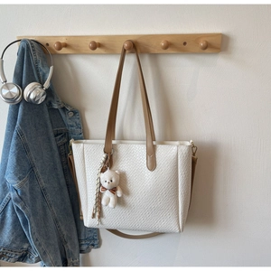 Detail of cream woven tote bag with brown leather straps and a plush bear charm hanging
