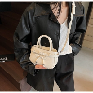 Close-up of white mini handbag with bow detail and star pendant worn by model