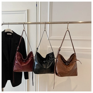Close-up of large glossy leather tote bags in burgundy, black, and brown displayed on a rack