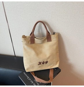 Detail of vintage beige canvas tote bag with brown embroidery and handles on black book
