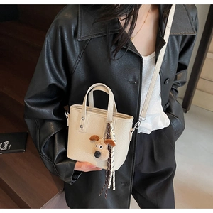 Detail of cream leather bucket bag with cute brown puppy charm and slim shoulder strap