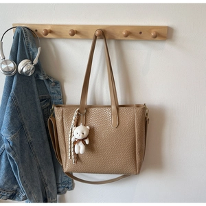 Detail of khaki woven tote bag with cute bear charm and striped scarf on a wooden hook