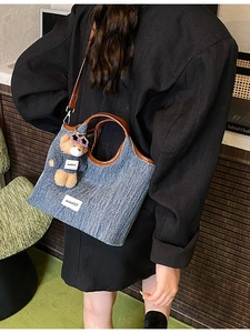 Denim tote bag with leather handles and teddy bear charm shown on a female model