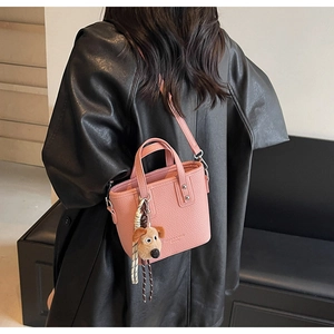 Detail of pink lychee grain crossbody bucket bag with a cute brown plush puppy pendant