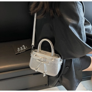 Detail of silver metallic handbag with bow accent and crossbody strap shown on model