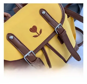 Detail showing yellow backpack flap with heart embroidery and brown leather straps