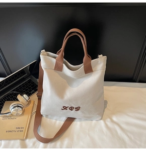 Detail of canvas tote bag showing brown leather handles and adjustable shoulder strap