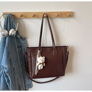 Detail of dark brown woven tote bag featuring a cute bear charm and adjustable strap