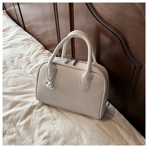 Detail of cream lychee texture leather bowling bag with silver puppy charm and zipper