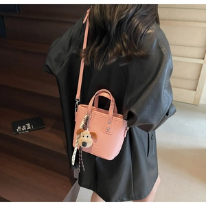 Pink bucket bag with plush charm and plaid scarf detail worn on a dark background