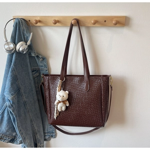 Detail of dark brown woven tote bag featuring a cute bear charm and silk scarf