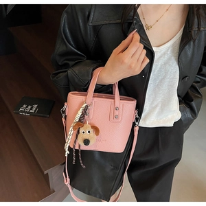 Pink bucket bag with lychee texture featuring a cute dog pendant and striped scarf detail