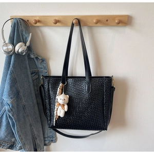Detailed view of black woven tote bag with a white bear charm hanging on a wooden rack