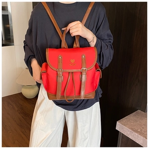 Detail of red nylon backpack with flower embroidery and brown leather trim on model