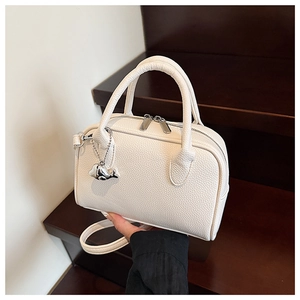 Close-up of white lychee texture leather bowling bag with silver whale charm and dual zipper