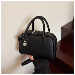 Close-up of black lychee texture leather bowling bag with silver bear charm and dual zipper