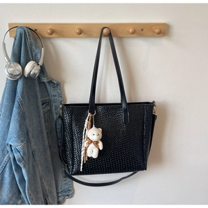 Detail of black woven tote bag featuring decorative plush bear charm and striped scarf