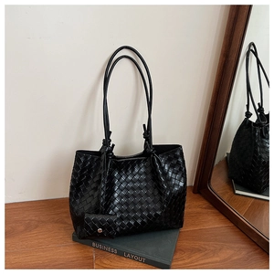 Detail view of large black woven tote bag and mini pouch set on a dark book
