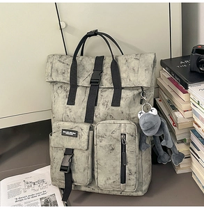 Detail of grey marble canvas backpack with roll-top buckle and frog plush keychain