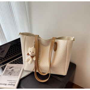Close-up of woven texture cream tote bag with cute bear charm and laptop background