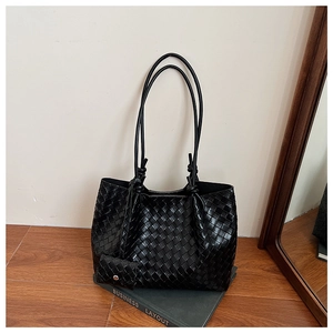 Detail of black woven leather tote bag with knotted straps resting on a green book